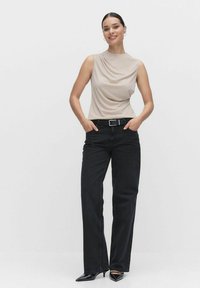 Beige ærmeløs top med draperet halsudskæring, parret med højtaljede sorte vide jeans og sorte spidse hæle. Sort bælte detalje synlig.
