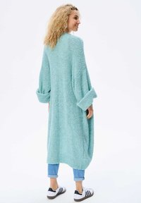 Jasnoniebieski, oversize sweter z dzianiny, z długimi rękawami, teksturowany materiał i ściągacz u dołu, zestawiony z podwiniętymi dżinsami i trampkami.