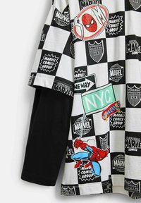 T-shirt med kort ärm i svart-och-vitt rutmönster med Spider-Man och olika serietidningslogotyper; har färgglada tryckta detaljer.