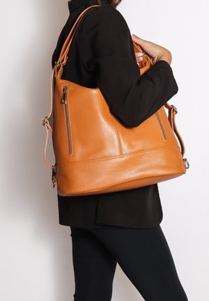 Grand sac à main en cuir orange avec une finition texturée, doté de deux poches zippées sur les côtés et d'une longue bandoulière réglable.