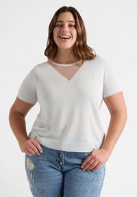 Jasnoszary, krótki top z rękawami, z dekoltem w serek i przezroczystą wstawką przy dekolcie. Posiada dekoracyjne przeszycia wzdłuż brzegów oraz miękką fakturę.
