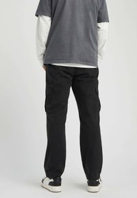 Pantalons cargo noirs décontractés avec poches latérales, poignets élastiques et un t-shirt gris assorti porté par-dessus une chemise blanche à manches longues.