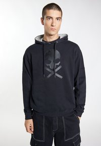 Zwarte hoodie met een geëxtrudeerd doodskop- en bottenmotief op de voorkant. Heeft een capuchon met trekkoord en een relaxed fit.