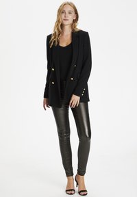Černý dvouřadý blazer se zlatými knoflíky, v kombinaci s lesklými černými legínami a černými lodičkami na otevřenou špičku. Hladká tkanina, přiléhavý střih.