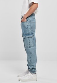 Světle modré cargo kalhoty vyrobené z denimu. Obsahují elastické manžety, boční kapsy a volný střih. Nosené s bílými teniskami.