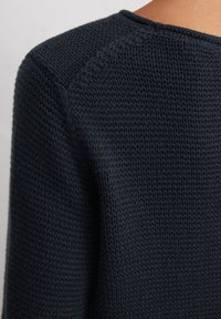 Navyblauer Strickpullover mit strukturiertem Gewebe und rundem Ausschnitt. Das Design umfasst Raglanärmel und subtile Nähdetails.
