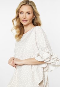 Blusa beige chiaro con motivo a pois, caratterizzata da maniche arricciate e vestibilità rilassata. Texture morbida, scollo tondo.