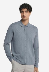 Ljusblå långärmad polo skjorta i mjukt tyg, med knäppning fram, krage och en avslappnad passform.