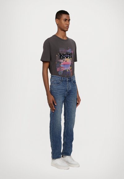 Graues T-Shirt mit kurzen Ärmeln und buntem Grafikdesign, kombiniert mit blauen Jeans und weißen Sneakers. Lässiger Schnitt und klassischer Denim-Stil.