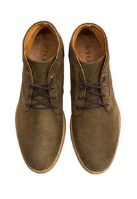 Brązowe zamszowe buty na sznurowadła z okrągłym noskiem, kontrastującą jasną podeszwą i ciemnymi sznurowadłami. Wnętrze wykończone jest beżową podszewką.