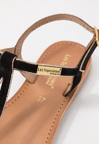 Black suede sandal with a gold-tone hardware detail. Features a tan leather insole with embossed branding and size 37. Minimalist design.