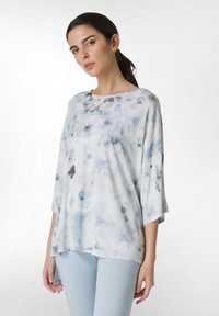 Vaaleansininen kukkakuosiset toppi, joka on valmistettu pehmeästä kankaasta, laajalla venekauvalla ja kolmanneksen pituisilla hihoilla, yhdistettynä vaaleansinisiin legginsseihin.