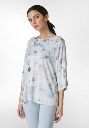 Lyseblå blomstret top lavet af blødt stof med en bred bådudskæring og trekvartærmer, sat sammen med lyseblå leggings.