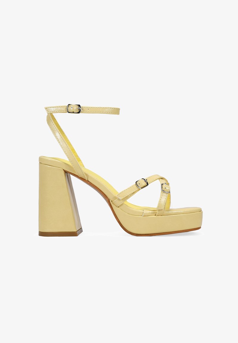 Sandalia de tacón alto de charol amarillo con un tacón cuadrado, correa de tobillo ajustable y correas frontales entrelazadas, que cuenta con una plataforma.