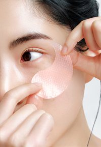 Patch oculaire en gel appliqué sous l'œil, rose semi-transparent avec une surface texturée. Peau lisse et cheveux foncés visibles.