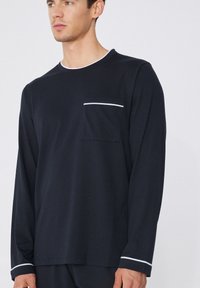 Camisa de manga larga en color navy, fabricada en tejido suave con cuello redondo, que presenta un acento blanco en el cuello y un bolsillo en el pecho con una franja blanca.