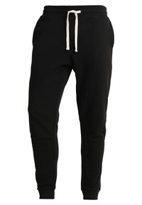 Black sweatpants made from soft fabric, featuring an elastic waistband with a cream drawstring, tapered ankles, and side pockets.
