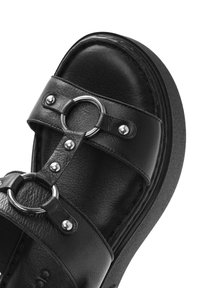 Sandal in pelle nera con doppie cinghie e dettagli in metallo argentato, anello circolare e soletta testurizzata su una suola piattaforma.