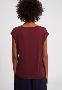 Bordeaux krátký rukáv top s uvolněným střihem, kulatým výstřihem a jemnou texturou. Má mírně zakřivený spodní lem a minimální designové prvky.