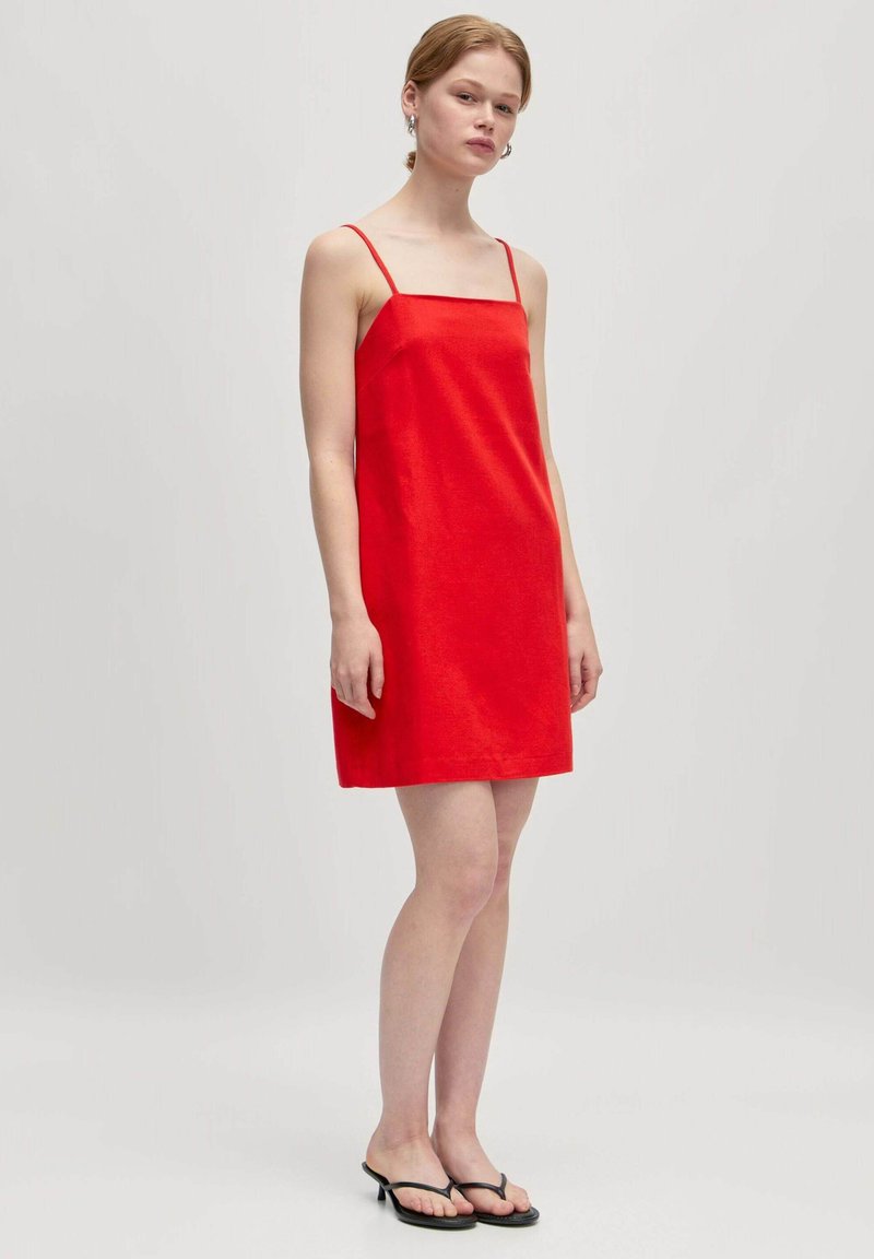 Rotes ärmelloses Kleid mit quadratischem Ausschnitt, geradem Schnitt und glatter Textur. Getragen mit schwarzen flachen Sandalen. Minimalistisches Design.