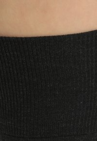 Leggings neri a coste che mostrano un tessuto lavorato a maglia, con linee verticali prominenti e una vita elastica per una vestibilità aderente.