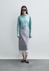 Světle modrá košile na knoflíky, šedá sukni s krajkovým lemem, černé ploché boty a nadměrné černé sluneční brýle; hladká tkanina a upravený střih.