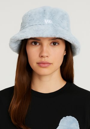 Helle blaue Kunstfell-Bucket-Hat mit breiter Krempe und glänzendem Logo-Detail an der Vorderseite; getragen mit einem schwarzen T-Shirt.