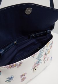 Taske med blomsterdesign, hvid yderside og marineblå inderside. Har en magnetlukning og en lynlåslomme til sikker opbevaring.