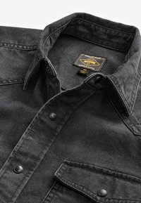 Black denim shirt with a button-down collar, featuring a chest pocket and black snap buttons. Durable fabric with a structured design.