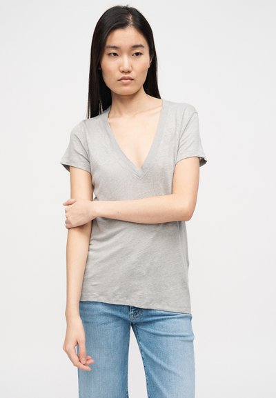T-shirt cinzento de manga curta com decote em V, em tecido macio e leve, com corte descontraído e textura subtil. Usado com jeans azul claro.
