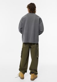 Un sweat-shirt gris surdimensionné avec des épaules tombantes, associé à un pantalon cargo vert olive avec des poches latérales, et des bottes beiges.