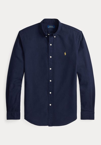 Tamsiai mėlyni ilgarankoviai marškiniai su sagomis, sagotu apykakle ir mažu geltonu Polo Ralph Lauren logotipu kairėje krūtinės pusėje.