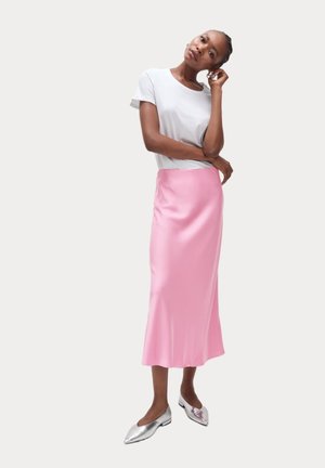 Jupe midi en satin rose avec un léger éclat, associée à un t-shirt blanc à manches courtes et des ballerines argentées à bout pointu.