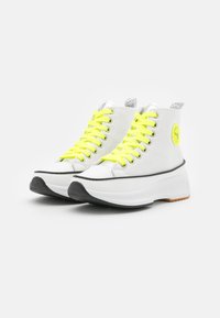 Witte hoge sneakers met neon gele veters, textielstructuur, zilveren accenten en een zwarte rubberen zool. Opvallend cirkelvormig logo aan de zijkant.
