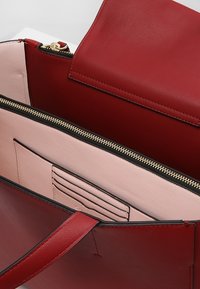 Sac à main en cuir rouge avec un design structuré, doté d'un intérieur rose pâle, d'une fermeture éclair noire et de fentes pour cartes internes.