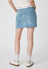 Falda de mezclilla azul claro con corte recto, dos bolsillos traseros y un dobladillo ligeramente deshilachado. Combinada con zapatillas blancas y calcetines texturizados.
