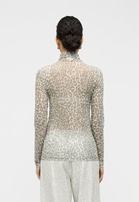Μπλούζα με μακριά μανίκια από διαφανές ύφασμα σε ανοιχτό πράσινο και μπεζ λεοπάρ σχέδιο. Διαθέτει ψηλό γιακά και απαλή υφή. Φοριέται με αντίστοιχο ανοιχτόχρωμο κάτω μέρος.