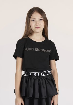 T-shirt nera con "JOHN RICHMOND" in strass, abbinata a una gonna nera a balze con una cintura a contrasto decorata con stelle.