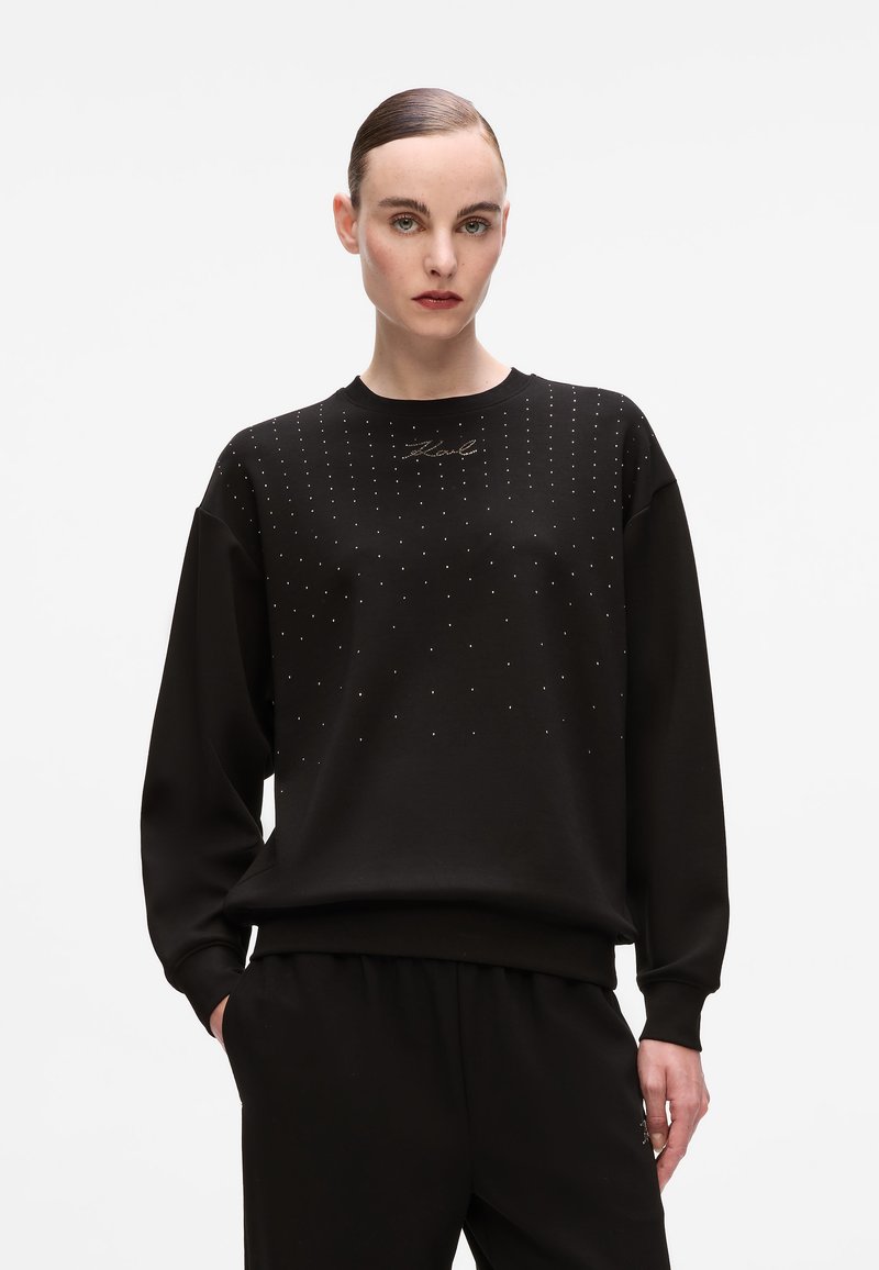 Sweatshirt preto com decote redondo e mangas longas. Decorado com pequenas tachas brilhantes e um bordado da marca na parte frontal.