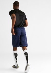 Athletic shorts in navy blue, fitted black t-shirt, knee-high white socks with black geometric pattern, and grey sports shoes with accents.