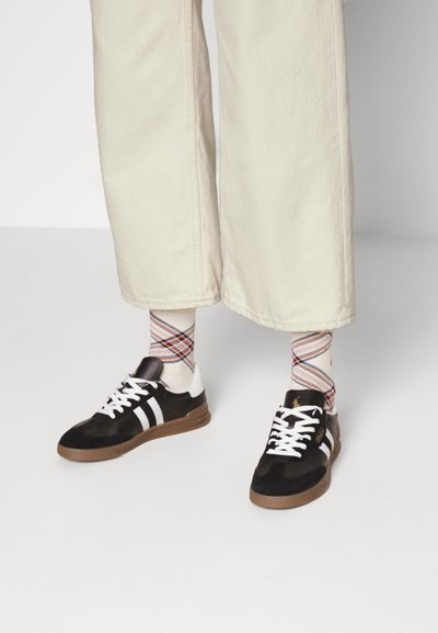 Czarno-białe trampki z gumową podeszwą, z zamszową cholewką, trzema paskami i w połączeniu z wzorzystymi skarpetkami do kolan.