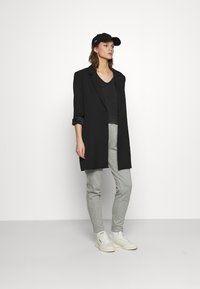 Melna garā žakete virs tumšā tops, pelēki sporta bikses un baltas kedas. Melns beisbola cepure papildina outfitu. Gludas auduma faktūras.