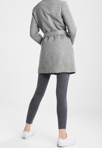 Abrigo gris de mezcla de lana con cintura ceñida, combinado con leggins gris oscuro y zapatillas blancas. Textura suave, diseño hasta la rodilla.