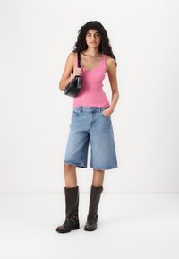 Lys rosa ribbet tanktop, blå denimshorts med løs passform, brune knelange støvler og en liten svart skulderveske.