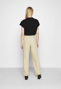 Polo shirt noir à manches courtes, pantalons beiges taille haute et chaussures à talons carrés noires. Tissu lisse, coupe ajustée, design minimaliste.