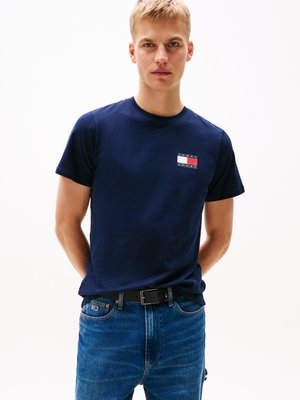 Marinblå bomulls t-shirt med kort ärm, med en rektangulär logotyppatch på bröstet. Tillverkad i kombination med blå denimjeans och ett svart bälte.