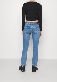 Černý zkrácený top s dlouhým rukávem v kombinaci se světle modrými rovnými džíny, které mají zadní kapsy a hnědou koženou nášivku, doplněné černými teniskami.