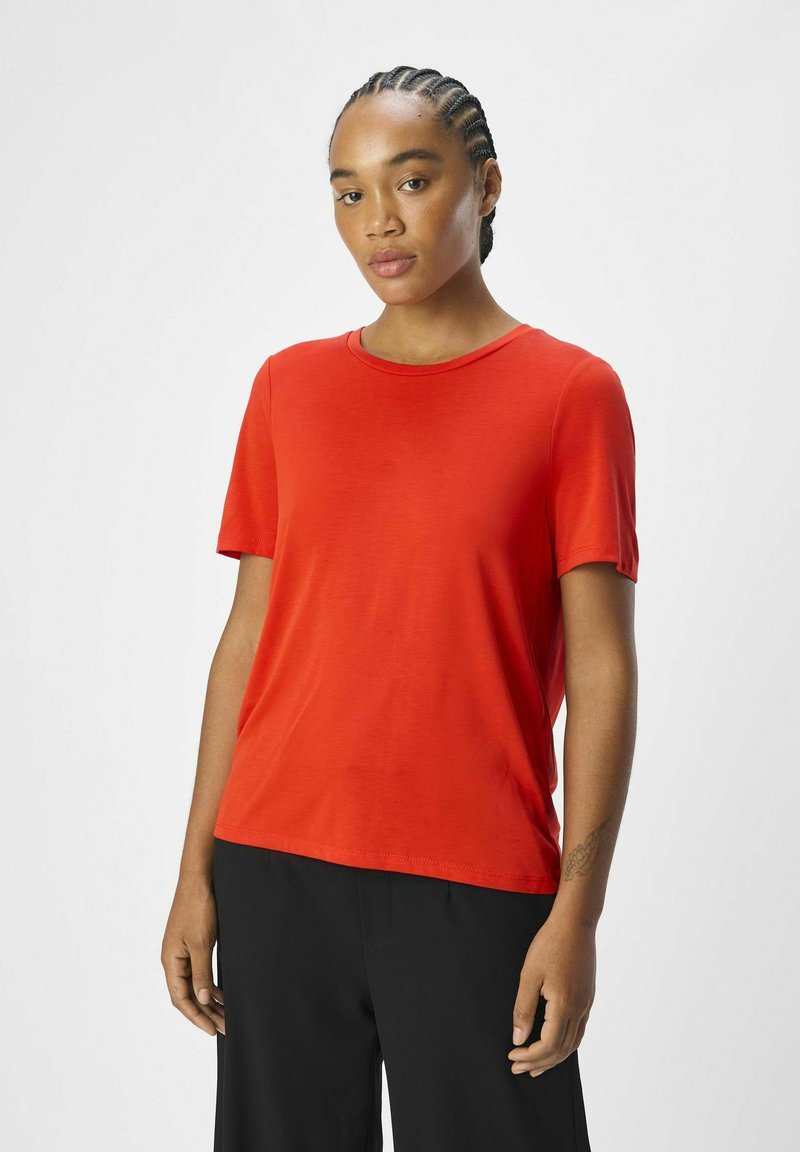 Rød kortærmet t-shirt, rund hals, blødt stof, afslappet pasform. Båret med sorte bukser, der viser et enkelt design uden mønstre eller udsmykninger.
