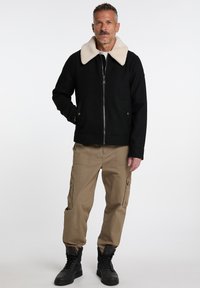 Black jacket with a soft beige shearling collar, front zipper, and side pockets, paired with beige cargo pants and black boots.