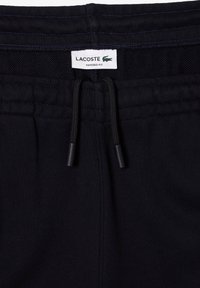 Čierne tapered fit teplákové nohavice s elastickým pásom, čiernymi šnúrkami a bielou nášivkou Lacoste so zeleným logom krokodíla.